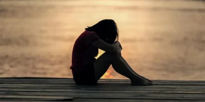 female sat by the lake at sunset appearing to be worried
